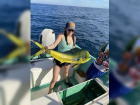 A joyful angler proudly displays her catch aboard a fishing boat, capturing the thrill of a successful day on the water.