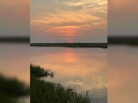A stunning sunset reflects on calm waters, creating a picturesque scene perfect for nature lovers and photographers.