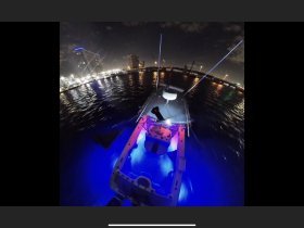 A sleek speedboat illuminated with colorful lights, set against a vibrant city skyline at night — perfect for evening cruises and fishing adventures.
