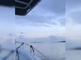 A serene view from the bow of a boat, showcasing calm waters and a distant shoreline under a cloudy sky — perfect for tranquil boating experiences.