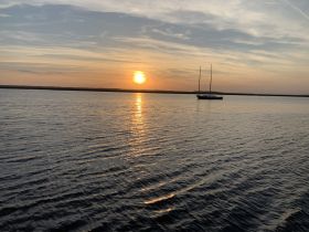 A serene sunset view featuring a sailboat anchored in calm waters, creating a picturesque scene perfect for relaxation and reflection.