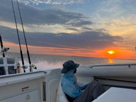 A serene sunset view from a fishing boat, with a lone angler enjoying the tranquil ocean atmosphere — perfect for fishing enthusiasts and sunset lovers.
