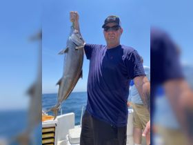 A proud angler displays his impressive catch aboard a fishing boat, showcasing the thrill of deep-sea fishing in the open ocean.