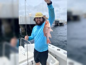 A man proudly displays his catch of the day, a vibrant fish, while aboard a fishing boat — a perfect moment for fishing enthusiasts.