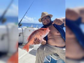 A joyful angler proudly displays his catch of the day, a vibrant red snapper, while enjoying a fishing trip on the open water.