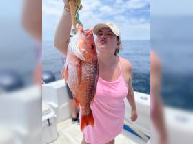 A joyful angler proudly displays her catch of the day, a vibrant red snapper, while enjoying a fishing trip on the open water.
