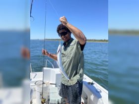 A joyful angler proudly displays his catch aboard a boat, capturing the excitement of a successful fishing trip on the water.