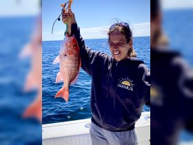 A joyful angler proudly displays her catch of the day, a vibrant red snapper, while enjoying a day out on the open ocean.