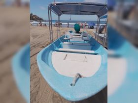 A view of a small blue boat on the beach, with people enjoying the sun and surf in the background, perfect for beachside adventures.