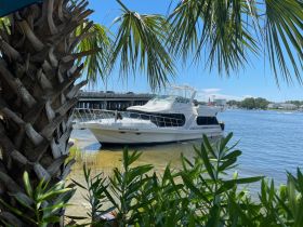 A picturesque view of the 'Nauti Pleasure' yacht docked by the shore, surrounded by lush greenery and clear waters, perfect for a relaxing day on the water.