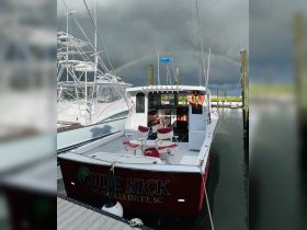 The 'Side Kick' boat is docked at Murrells Inlet, SC, showcasing its vibrant design against a backdrop of stormy skies and a rainbow.