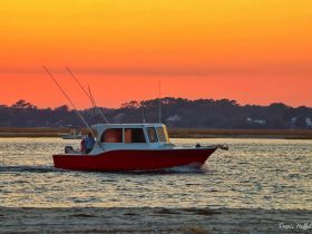 A fishing boat navigates through tranquil waters at sunset, creating a picturesque scene perfect for evening excursions.