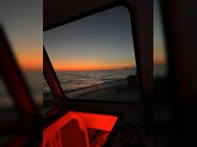 A serene view from inside a boat's cabin, showcasing a stunning sunset over the water, illuminated by soft red lighting.