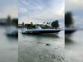 A sleek speedboat is docked in shallow waters, showcasing its vibrant design against a serene backdrop of palm trees and a clear sky.