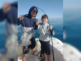 A father and son proudly display their catch while fishing together on a beautiful day at sea, capturing a memorable bonding experience.