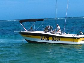 A sleek speedboat named 'Black Moon' is seen cruising through clear waters, showcasing its vibrant design and fishing gear.