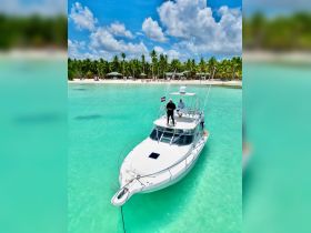 Aerial view of a boat anchored in crystal-clear waters, with two crew members on deck, showcasing a perfect tropical getaway.