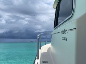 A side view of a Parker 2820 XL boat cruising through clear turquoise waters, showcasing its sleek design against a backdrop of dramatic clouds.