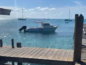 A picturesque view of a small boat docked in clear turquoise waters, with sailboats in the background, perfect for a serene day on the water.