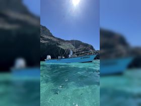 A clear view of the boat 'LA CHIMANGO' anchored in pristine turquoise waters, surrounded by rocky cliffs — perfect for exploring coastal destinations.