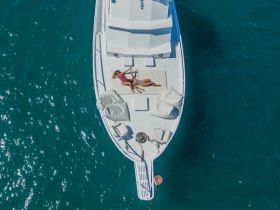 Aerial view of a woman relaxing on the deck of a boat, soaking up the sun on tranquil waters — an ideal scene for leisure and relaxation on the water.