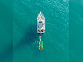 A lively group enjoys a fun day on the water, swimming and relaxing on a floating mat beside a boat — perfect for summer adventures and family outings.