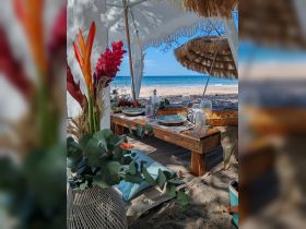 A beautifully arranged beach dining setup featuring fresh food and drinks, perfect for a relaxing day by the ocean.