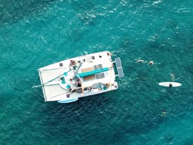 Aerial view of a lively group enjoying water activities around a catamaran, showcasing the fun of swimming and relaxation in the beautiful turquoise waters.
