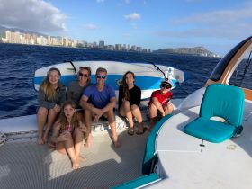 A joyful family poses on the deck of a boat with the stunning Diamond Head in the background, capturing a memorable moment in Hawaii's beautiful waters.