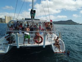 A lively group enjoys a day on a catamaran in Hawaii, with guests celebrating and swimming in the beautiful waters, creating unforgettable memories.