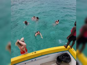 A lively group enjoys a refreshing swim in crystal-clear waters, with a boat visible in the background — perfect for a fun day on the water.