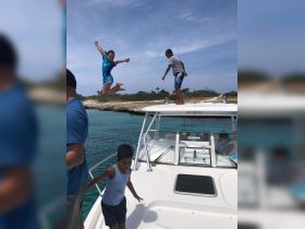 A group of kids enjoys a thrilling moment on a boat, with one child joyfully jumping into the water, capturing the essence of summer fun and adventure on the water.