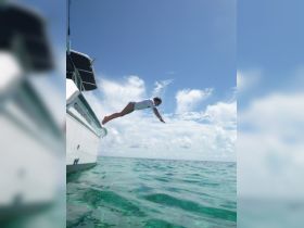 A young girl joyfully leaps off the back of a boat into the clear turquoise waters, capturing the thrill of summer fun and water activities.