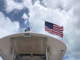 A striking view of a boat's bow with an American flag waving against a backdrop of blue skies and clouds, showcasing the vessel's exterior.