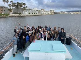 A vibrant group of friends gathers on a boat, celebrating together against a scenic waterfront backdrop — perfect for memorable outings and gatherings.