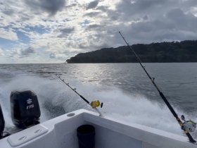 A fishing boat speeds through the ocean, showcasing fishing rods in action against a backdrop of dramatic clouds and a distant shoreline — perfect for adventure seekers and fishing enthusiasts.