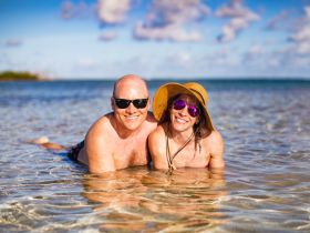 A joyful couple enjoys a sunny day at the beach, lounging in shallow waters — perfect for romantic getaways or fun beach days.
