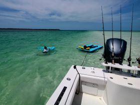 A child enjoys floating in shallow waters while another person relaxes on a mat nearby, showcasing a fun day on the water.