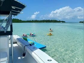 A family enjoys a sunny day in clear waters, with children floating and playing while the boat serves as a perfect backdrop for their fun-filled adventure.