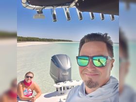A couple enjoys a sunny day on their boat, capturing a selfie with a stunning beach backdrop — perfect for memorable adventures on the water.