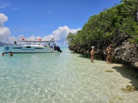 Guests enjoy a sunny day at the beach with a boat anchored nearby, perfect for swimming and snorkeling adventures in crystal-clear waters.