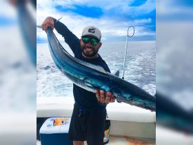A proud angler displays his impressive catch aboard a fishing boat, showcasing the thrill of deep-sea fishing in the open ocean.