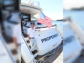 A smiling individual poses on the deck of the yacht 'Propensity' in Destin, FL, showcasing the American flag — a perfect representation of luxury boating experiences.
