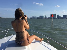 A woman captures the stunning city skyline while relaxing on the bow of a boat, showcasing the perfect blend of adventure and urban beauty on the water.