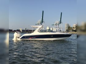 A sleek Formula speedboat docked in calm waters, showcasing its elegant design against a backdrop of urban scenery and cranes.