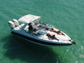 Two individuals relax and sunbathe on the deck of a boat in clear turquoise waters, showcasing the perfect setting for a day of leisure on the water.