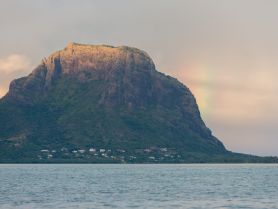 A stunning view of a mountain with a rainbow in the background, showcasing the natural beauty of the coastline — perfect for scenic boat tours.