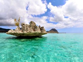A stunning view of a rocky outcrop surrounded by crystal-clear turquoise waters, showcasing the natural beauty of the coastline — perfect for island hopping adventures.