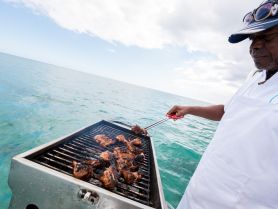 A chef expertly grills delicious chicken on a boat, showcasing the perfect BBQ experience on the water — ideal for catering and culinary adventures.