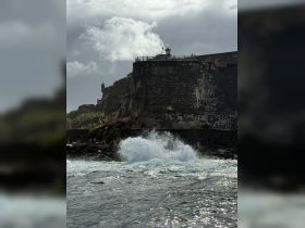 A stunning view of crashing waves against the rocky coastline, with a historic fort in the background, showcasing the beauty of coastal landmarks.